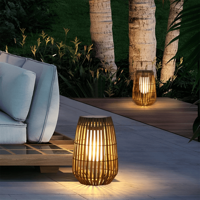 Two wooden lantern-style floor lamps glowing on a patio near a blue sofa and tropical greenery.