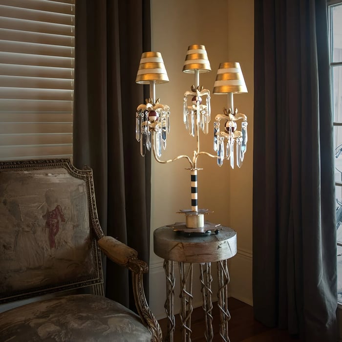 Classic table lamp with gold and crystal embellishments, placed on a wooden side table beside an ornate armchair in a traditionally styled room.