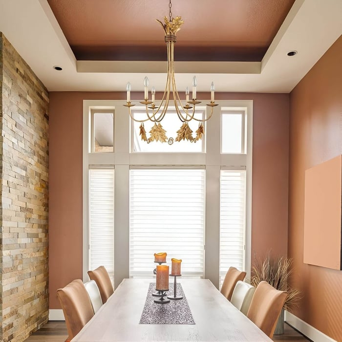 Warm-toned dining room with a gold leaf chandelier, tan chairs, and stacked stone accent wall.