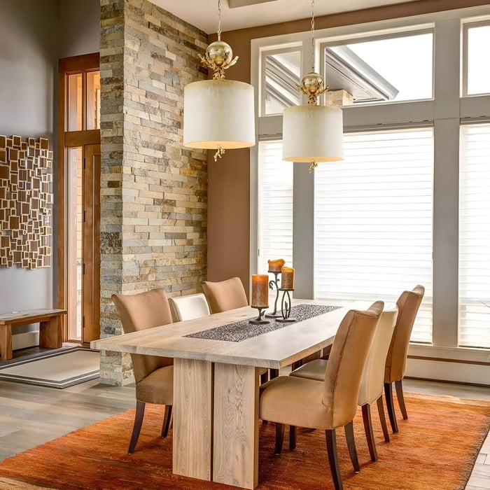 Warm dining room with stone accent wall, beige chairs, and two drum pendant lights.