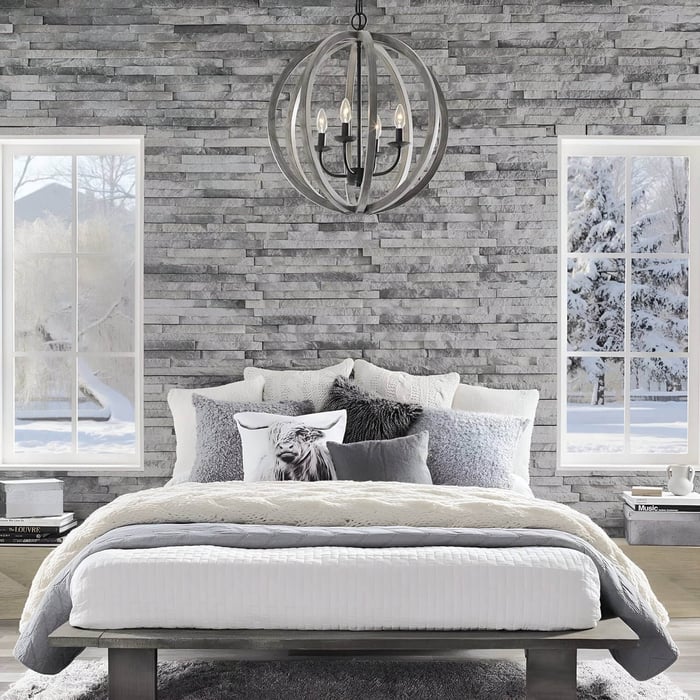 Modern bedroom with a stone accent wall, cozy layered bedding in gray and white tones, and a spherical metal chandelier hanging from the ceiling.