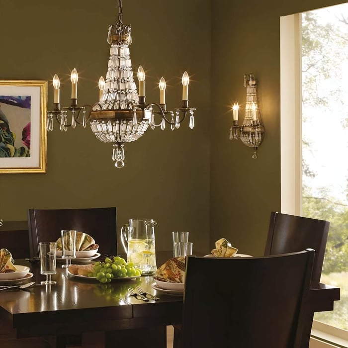 Traditional crystal and bronze chandelier over a dining table set with green walls.