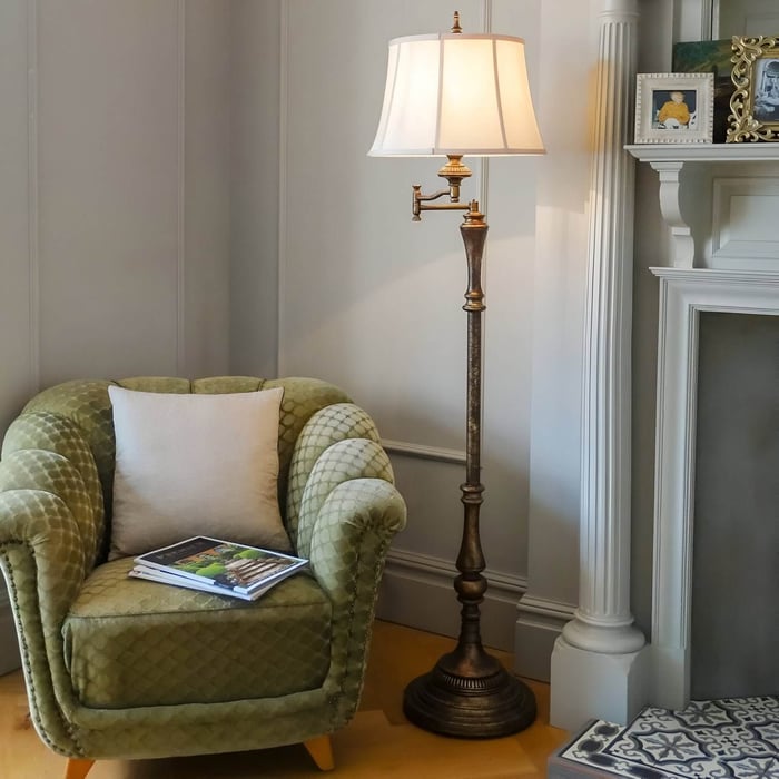 Antique brass floor lamp with swing arm and pleated shade positioned next to a green velvet armchair by a fireplace.