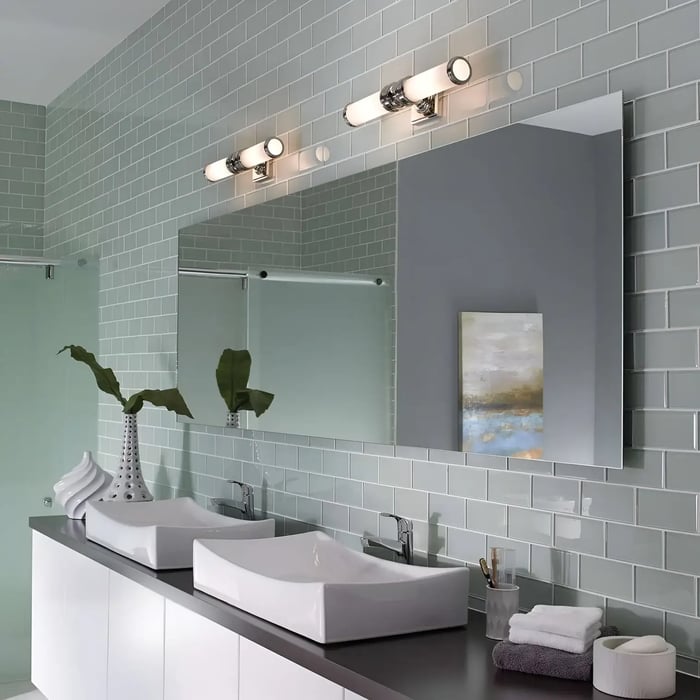 A double vanity setup with rectangular vessel sinks and a large wall mirror. Two modern light bars above provide balanced lighting. The mint green tiled backsplash, decorative vases, and neatly arranged towels give a fresh, spa-like feel.
