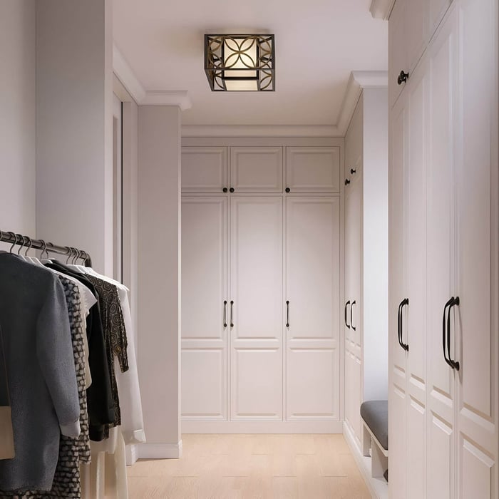 Walk-in closet with built-in cabinetry, hanging clothes, bench seating, and a square patterned flush mount ceiling light.