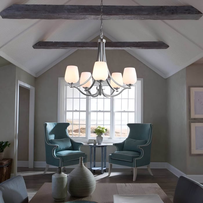 Vaulted ceiling sitting area with exposed beams, teal armchairs, and a brushed nickel chandelier light with white glass shades.