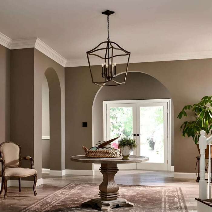 Open-frame lantern chandelier hanging in a neutral hallway above a round wooden table with double doors and arched doorway details.