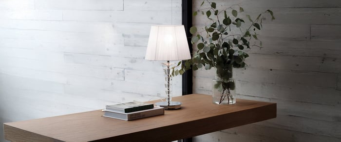Crystal table lamp with white shade on a wooden desk beside stacked books and a glass vase with greenery.