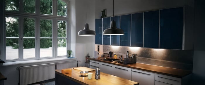 Modern kitchen with dark blue cabinets, wood countertops, and industrial pendant lights by large windows.