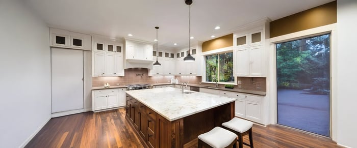 Bright kitchen with white cabinetry, a large central island, and three pendant kitchen lights hanging from the ceiling over the island.