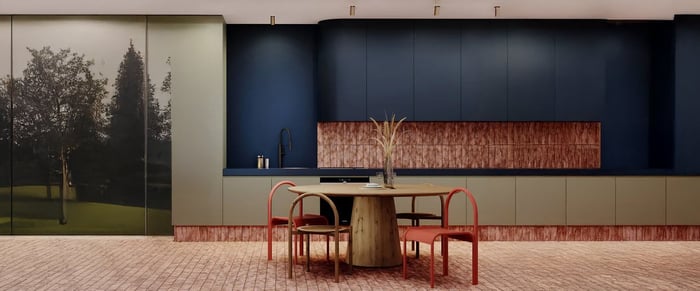 A contemporary kitchen featuring a bold navy and muted green colour palette and gold spotlights. A circular wooden dining table is surrounded by modern red chairs, with artistic use of copper accents on the backsplash and flooring.