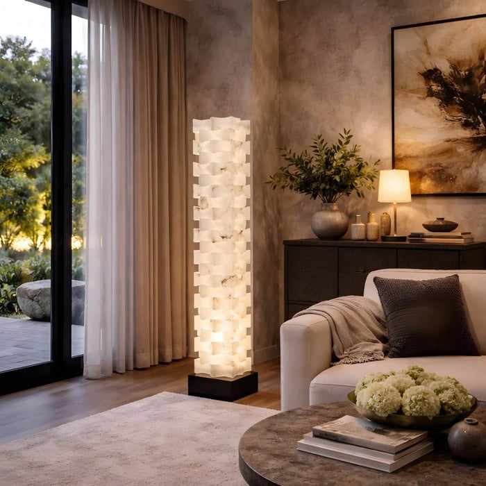 Cozy modern living room with warm ambient lighting, showcasing a tall sculptural floor lamp made of stacked translucent blocks beside a sofa and large glass doors opening to a garden.