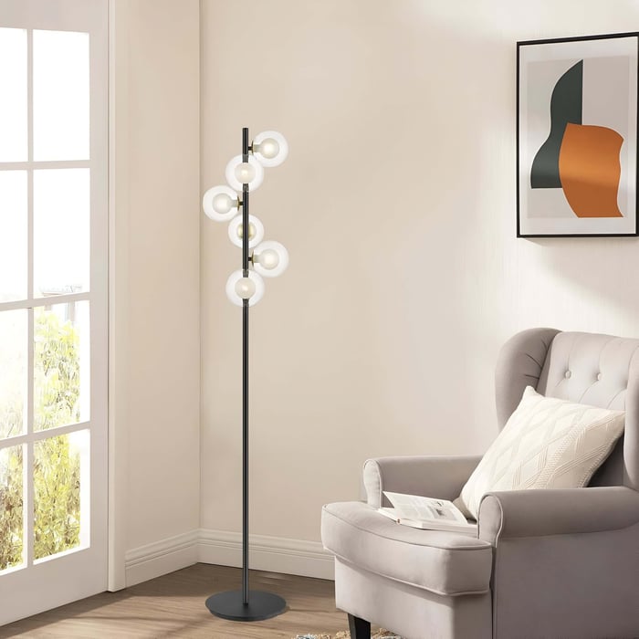 Black floor lamp with clustered circular globe lights beside a gray tufted armchair in a neutral living room with large window and abstract wall art.