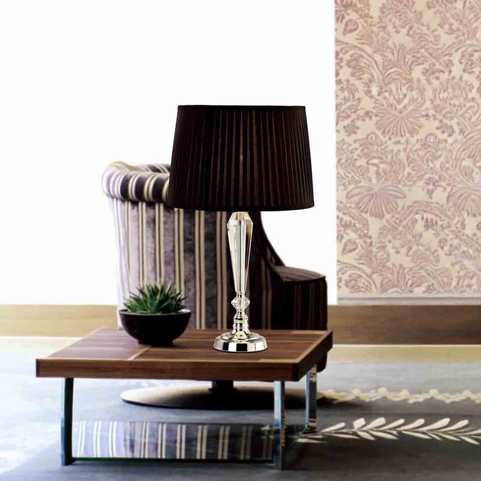 Crystal base table lamp with a black pleated shade on a wooden coffee table in front of a striped armchair.