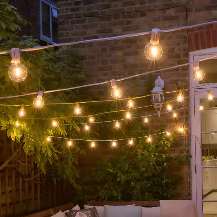 Outdoor string lights hung in parallel strands across a small brick courtyard with greenery and a warm wall lantern.