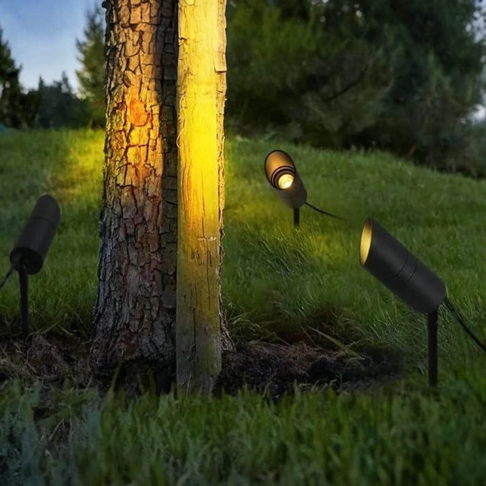 Outdoor spike spotlights uplighting a tree trunk in a grassy garden area.