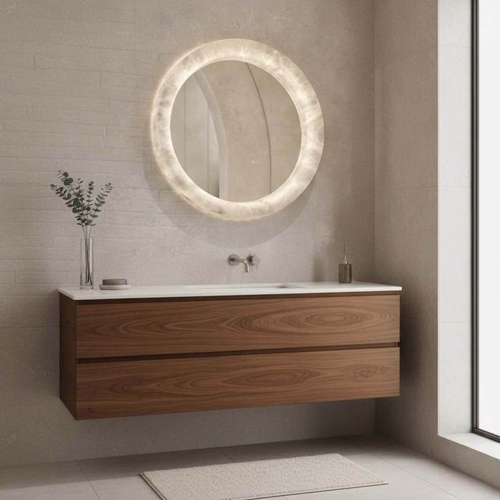 Round alabaster mirror with glowing translucent frame above floating wooden bathroom vanity.
