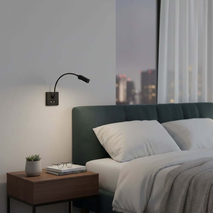 A modern living room with a gray sofa, wall-mounted black spotlight, wooden side table, stacked books, and a small succulent plant.