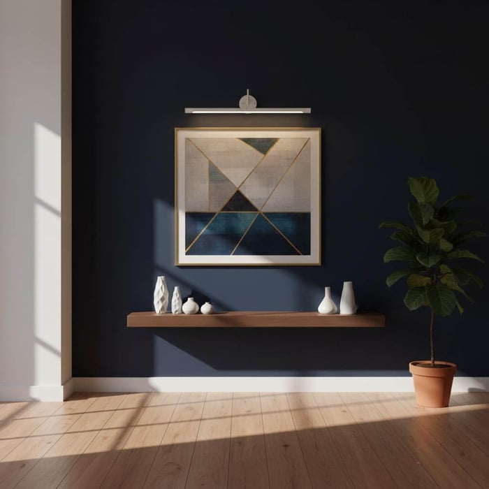 Modern framed abstract artwork lit by a picture light on a dark feature wall above a floating shelf and potted plant.