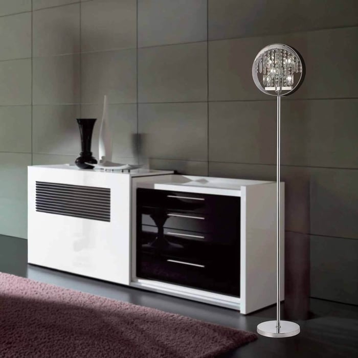 Slim chrome floor lamp with a round crystal shade beside a white sideboard in a contemporary grey-walled room.