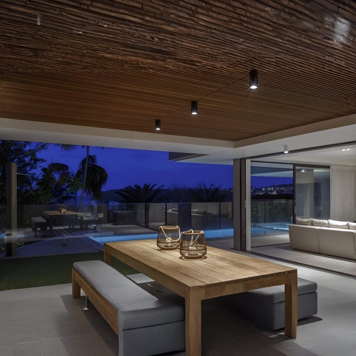 Small cylindrical downlights set into a timber slatted ceiling over a modern outdoor seating area at night.