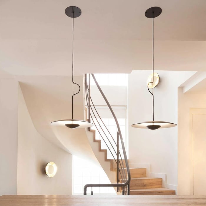 Minimal stairwell with two slim disc pendant lights hanging from long black cords in a bright white space.