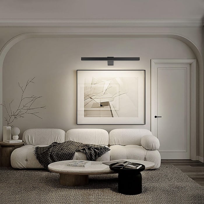 Neutral modern living room featuring a textured white sofa, abstract framed wall art, and a sleek black picture light mounted above the artwork.