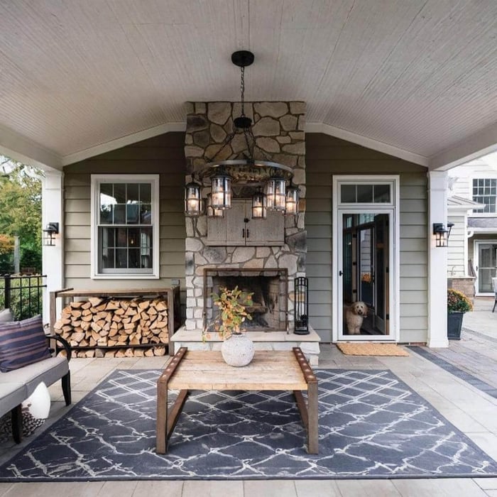 Lantern-style outdoor chandelier centred under a covered porch ceiling with stone fireplace and wall lights.
