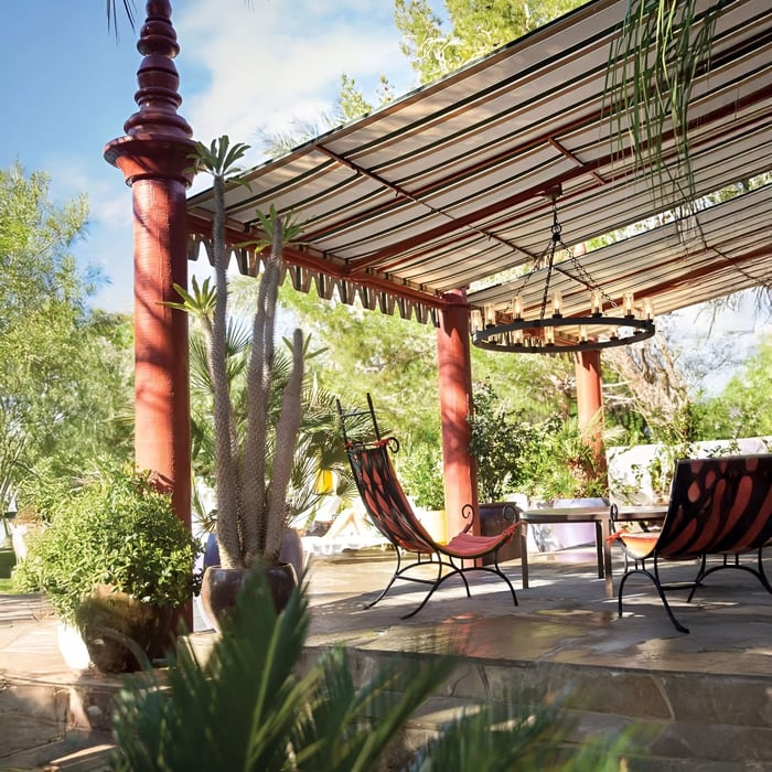 Large round wagon wheel chandelier with candle-style bulbs under a striped pergola in a tropical patio.