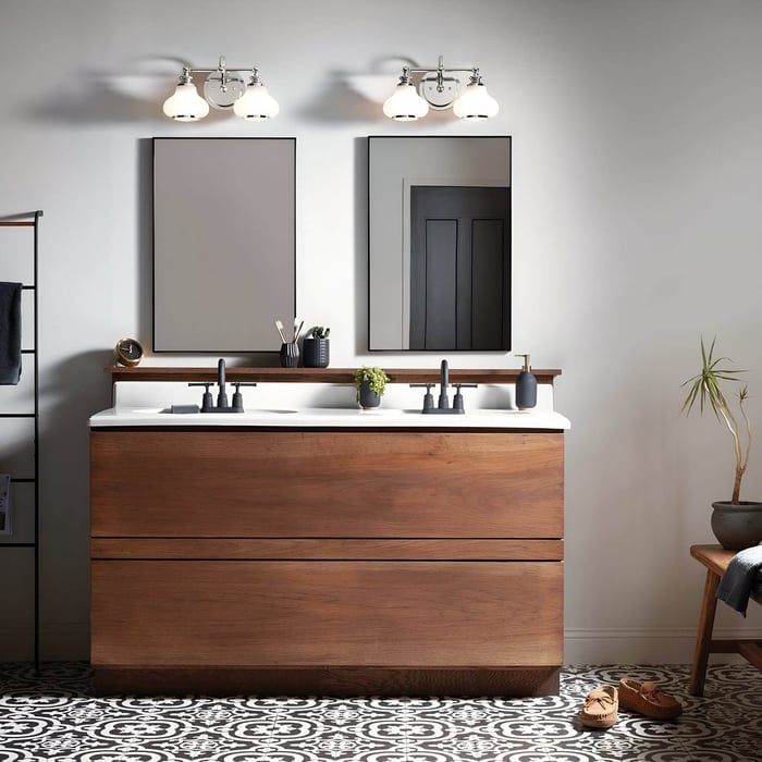 Contemporary bathroom with wooden vanity, twin mirrors, and vintage-style three-light fixtures with glass shades.