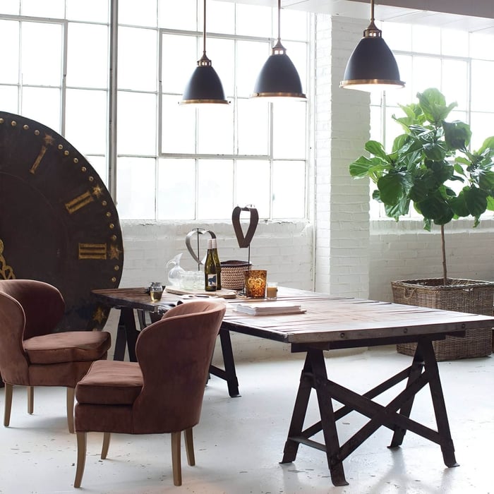 Industrial dining space with black pendant lights, rustic table, and large windows.