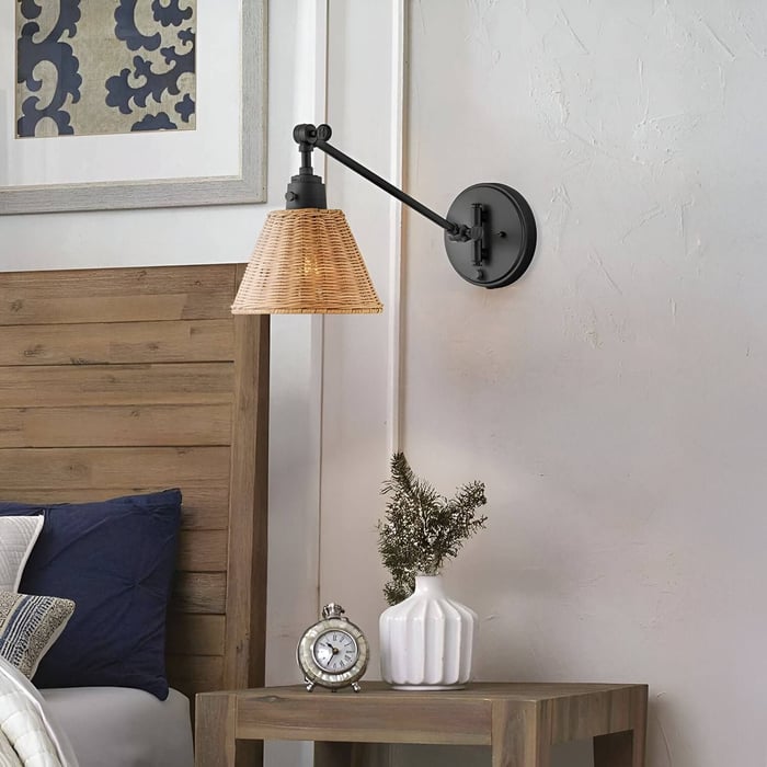 Adjustable wall-mounted lamp with a woven rattan shade above a wooden nightstand and bed.