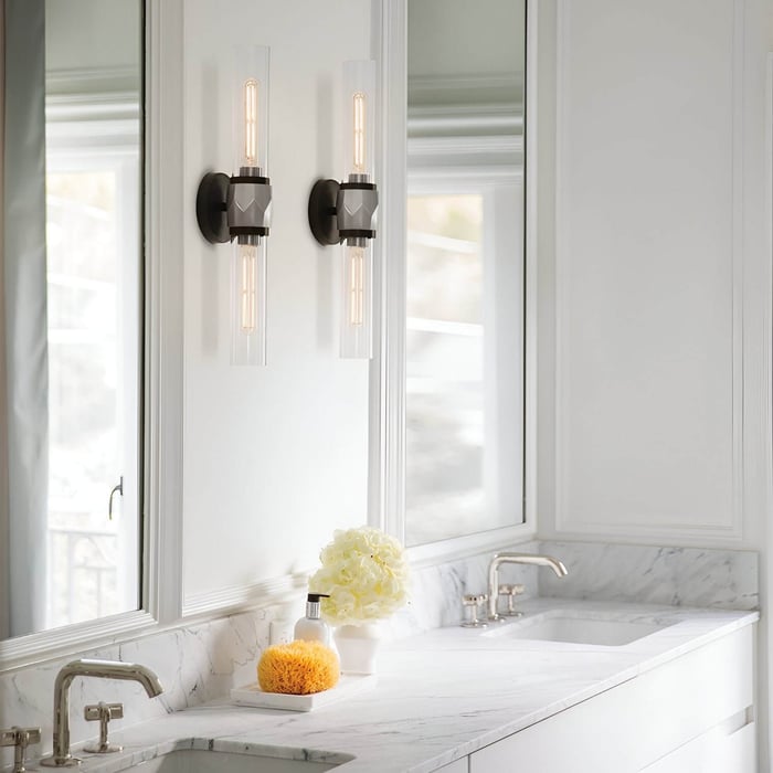White marble vanity with dual sinks and tall tubular sconces mounted vertically on each side of a mirror.