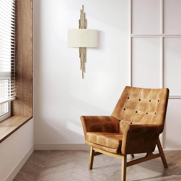 Textured gold wall sconce with linen shade above a caramel leather armchair in a bright corner with wood window seat.