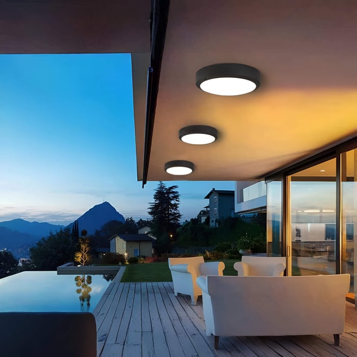 Three round surface-mounted ceiling lights under a modern overhang above an outdoor seating deck at twilight.