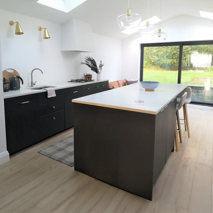 Minimalist black-and-white kitchen with island, brass wall sconces, and glass pendant lights overhead.