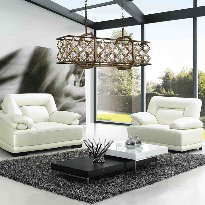 Bronze lantern-style linear chandelier with patterned crystal details in a modern living room with large windows and white sofas.
