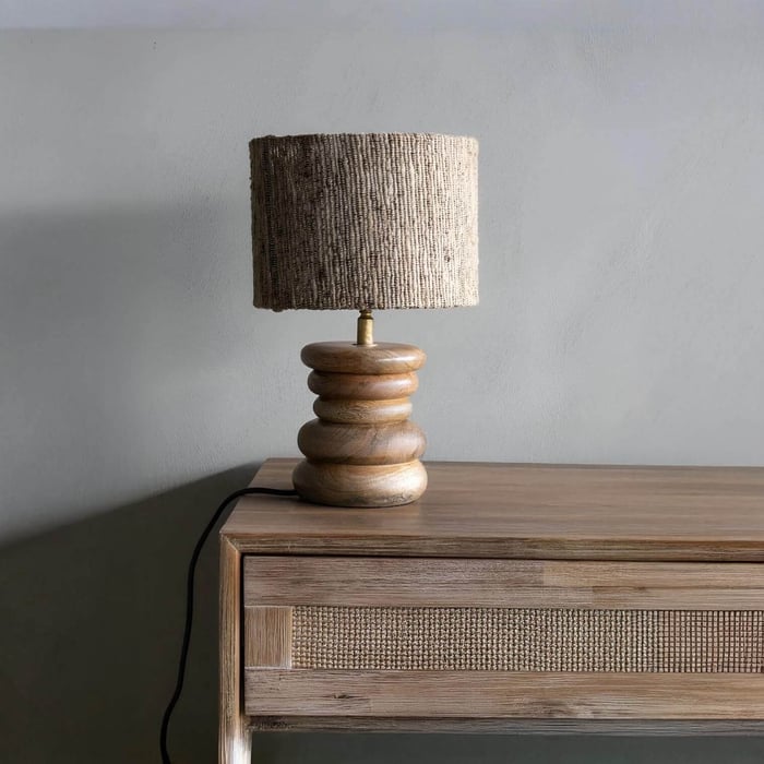Rustic wooden table lamp with a textured fabric shade on a matching wooden console against a neutral gray wall.