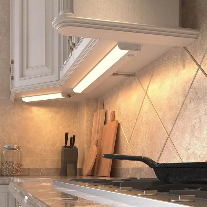 Warm under-cabinet LED bar light brightening a tiled backsplash above a kitchen hob.