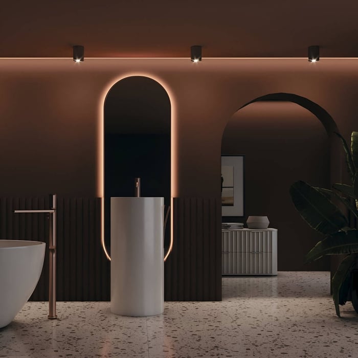Contemporary bathroom featuring black ceiling downlights and warm backlit arched mirror above pedestal sink.