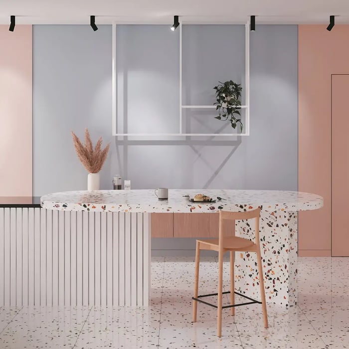 A stylish dining space showcasing a terrazzo-patterned table with rounded edges, paired with a simple wooden chair. Soft pastel pink and blue walls create a serene backdrop, enhanced by black track lighting.