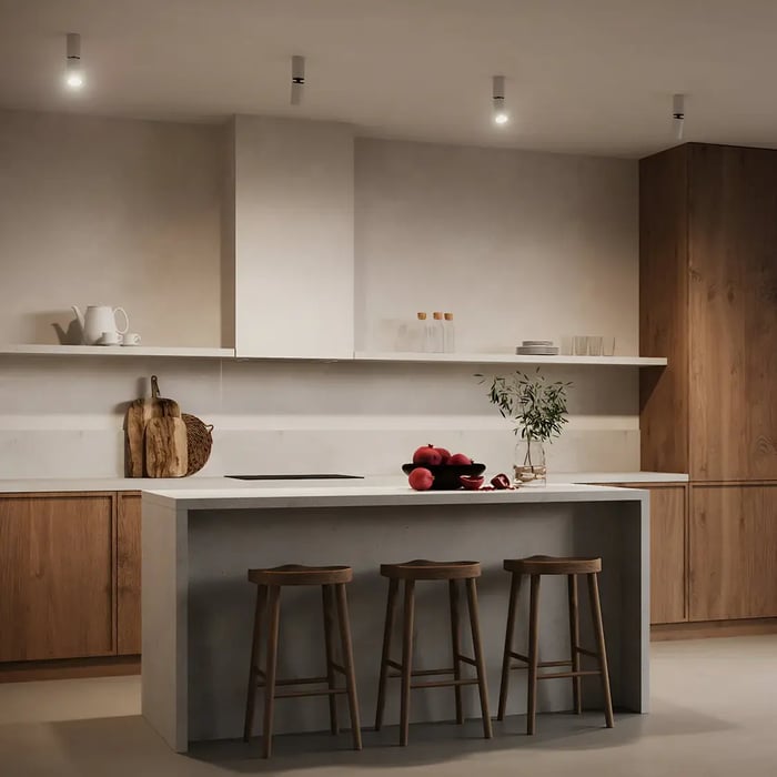 A warm minimalist kitchen featuring natural wood cabinetry and a concrete island. Modern white ceiling-mounted lights provide ambient illumination, while red apples and greenery add a pop of colour.