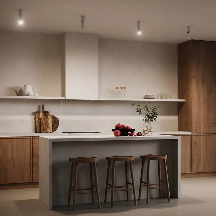Minimalist kitchen with four ceiling-mounted spotlights above a white island, warm wood cabinetry, and three bar stools.