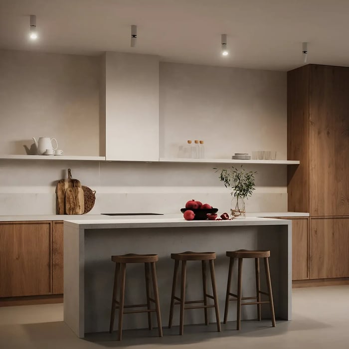 This serene, modern kitchen features a minimalist layout with light wood cabinetry and a sleek concrete island. Recessed kitchen lights create a soft glow that enhances the warm, earthy tones and clean architectural lines.