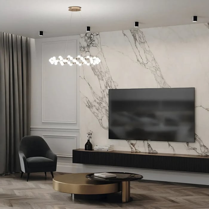 A stylish living room featuring recessed ceiling lights along with a modern chandelier above a sofa area. The marble wall behind the TV adds elegance to the space, while a contemporary coffee table and an accent chair complete the minimalistic design.