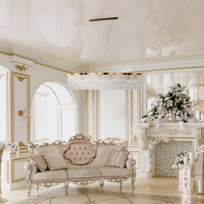 Ornate crystal chandelier in a white and gold classical room with carved sofa and floral decor.