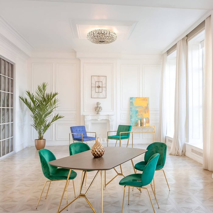 White-panelled room with low crystal ceiling fixture, vibrant velvet chairs, gold accents, and geometric patterned flooring.
