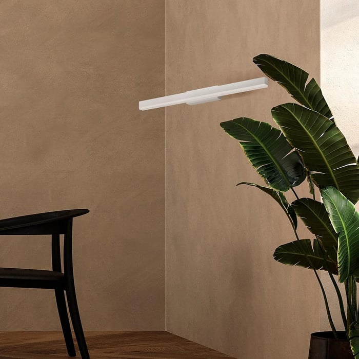 Minimalist white wall-mounted linear light on a beige textured wall beside a large green houseplant.