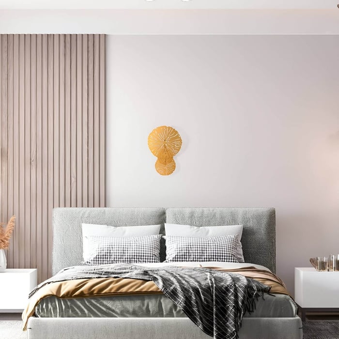 Minimalist bedroom with light gray upholstered bed, layered bedding, and a unique golden wall sconce shaped like abstract discs.