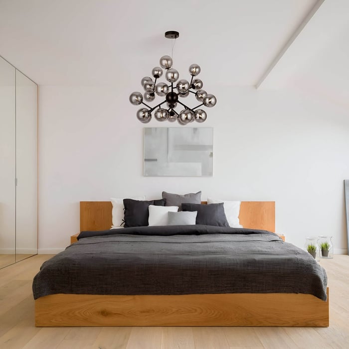 Modern bedroom with wooden bed frame, gray bedding, and a striking black chandelier with multiple metallic globe lights.